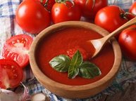 Een bord heerlijke tomatensoep op een tafel, met daar omheen verse tomaten en knoflook