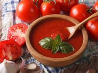 Een bord heerlijke tomatensoep op een tafel, met daar omheen verse tomaten en knoflook