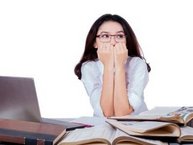 Een vrouw met examenvrees zit heel angstig achter haar laptop.